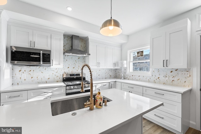 kitchen with hanging light fixtures, wall chimney range hood, light hardwood / wood-style floors, white cabinets, and appliances with stainless steel finishes