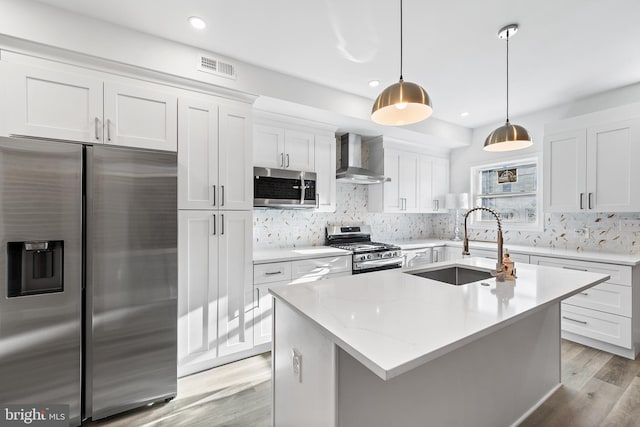 kitchen with sink, wall chimney exhaust hood, pendant lighting, white cabinets, and appliances with stainless steel finishes