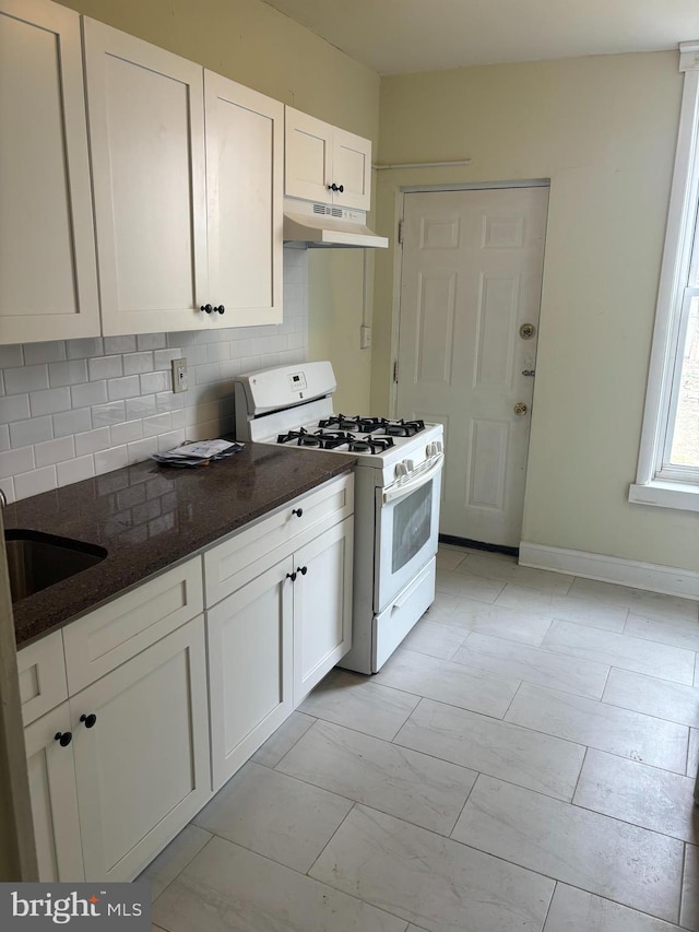 kitchen featuring sink, white gas range oven, decorative backsplash, dark stone countertops, and white cabinetry