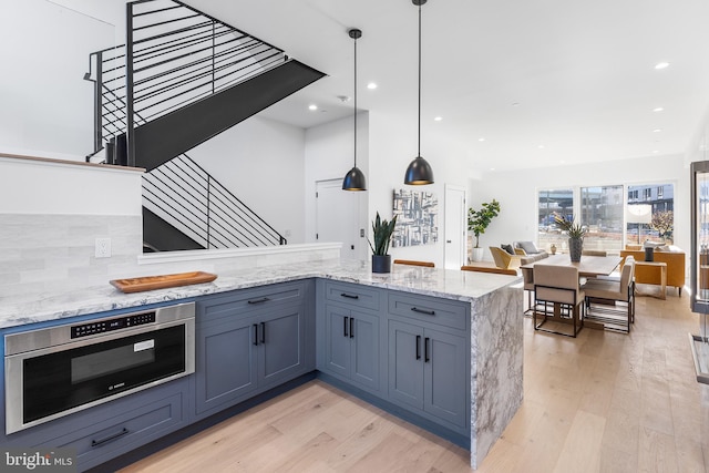 kitchen with tasteful backsplash, light stone countertops, decorative light fixtures, and light wood-type flooring