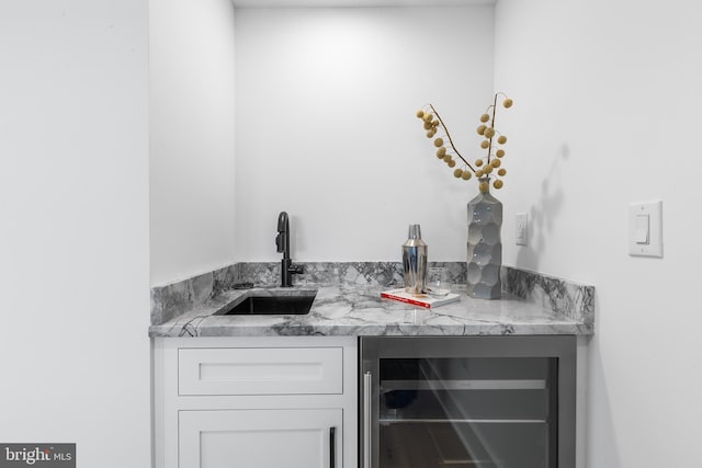 bar with white cabinets, light stone counters, beverage cooler, and sink