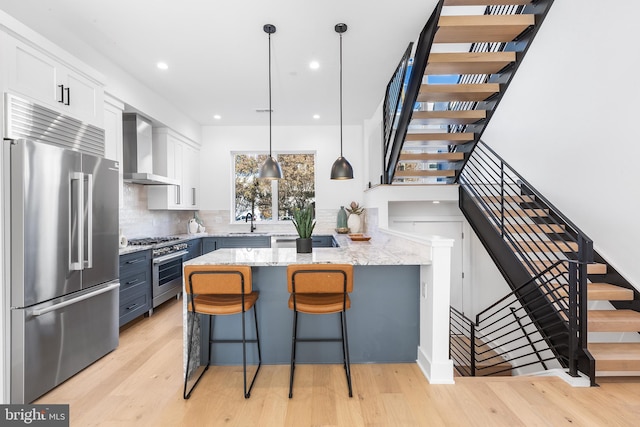 kitchen featuring white cabinets, light hardwood / wood-style floors, wall chimney exhaust hood, and high quality appliances