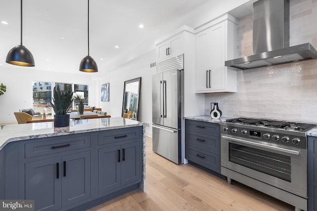 kitchen featuring white cabinets, wall chimney range hood, decorative light fixtures, premium appliances, and light hardwood / wood-style floors