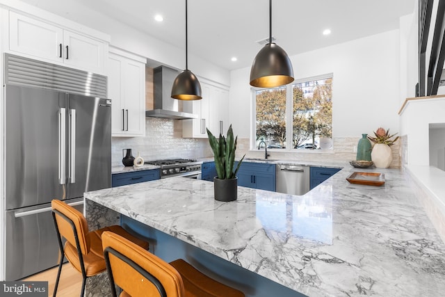 kitchen with white cabinets, a kitchen breakfast bar, wall chimney range hood, decorative light fixtures, and premium appliances