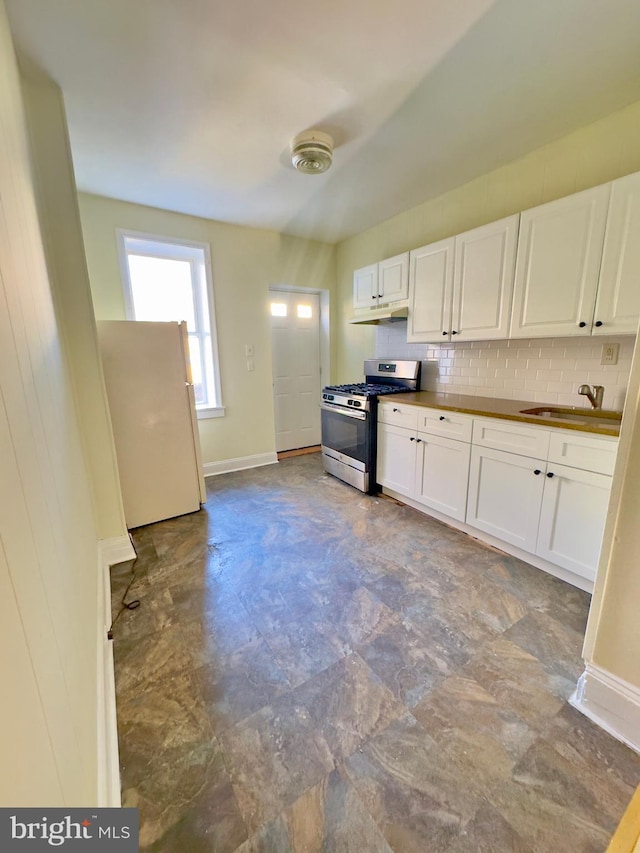 kitchen featuring sink, stainless steel gas range oven, white fridge, decorative backsplash, and white cabinets