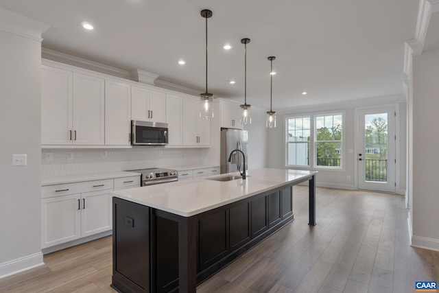 kitchen with pendant lighting, stainless steel appliances, white cabinetry, and an island with sink