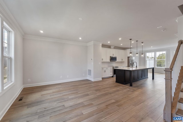 kitchen with white cabinetry, decorative light fixtures, a center island with sink, appliances with stainless steel finishes, and light wood-type flooring