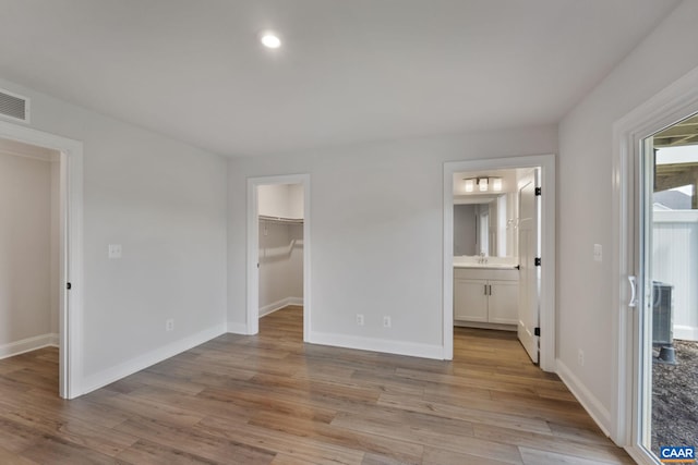 unfurnished bedroom featuring ensuite bathroom, sink, light wood-type flooring, a spacious closet, and a closet