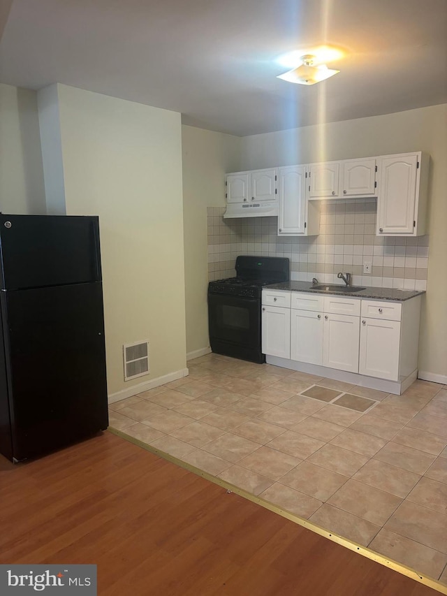 kitchen featuring tasteful backsplash, sink, black appliances, light tile patterned floors, and white cabinetry