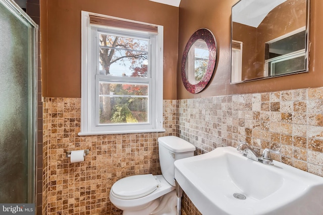 bathroom with an enclosed shower, toilet, sink, and tile walls