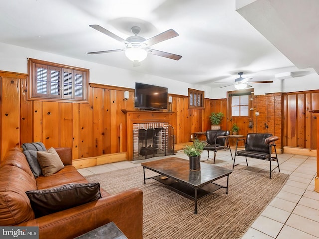 living room with a fireplace, light tile patterned floors, ceiling fan, and wood walls