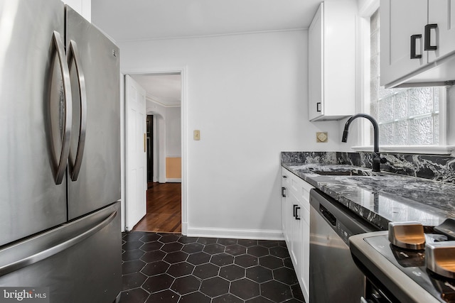 kitchen with appliances with stainless steel finishes, ornamental molding, sink, dark tile patterned flooring, and white cabinetry