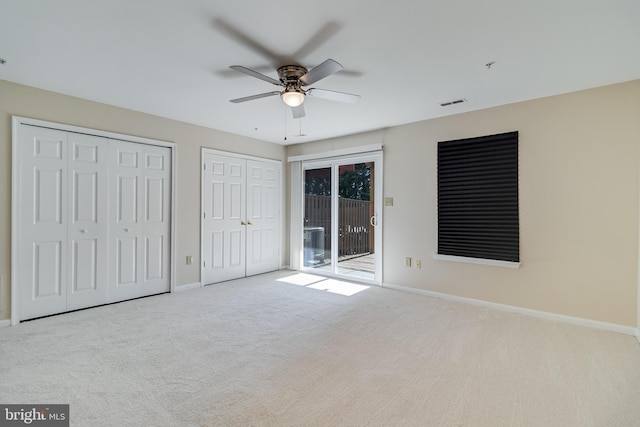 unfurnished bedroom featuring access to outside, ceiling fan, light colored carpet, and two closets