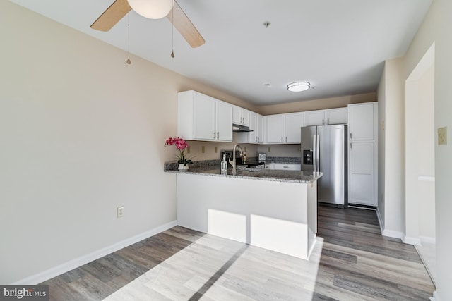 kitchen with kitchen peninsula, appliances with stainless steel finishes, dark stone countertops, white cabinets, and hardwood / wood-style floors