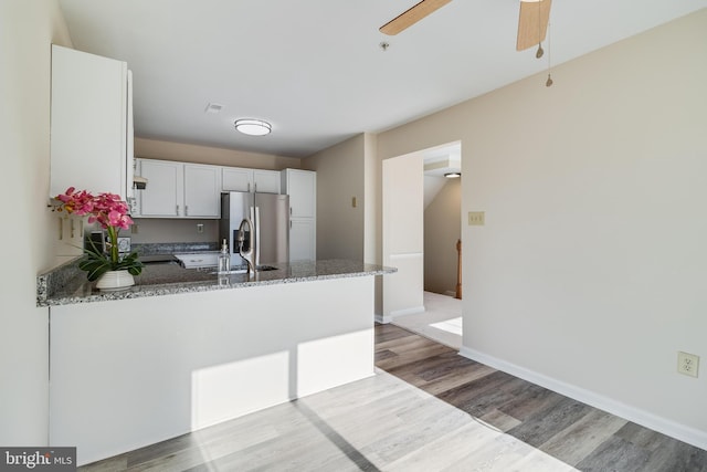 kitchen featuring kitchen peninsula, light hardwood / wood-style flooring, white cabinetry, and dark stone counters