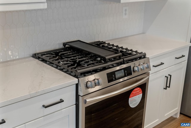 kitchen with gas stove, light stone counters, white cabinets, and light wood-type flooring