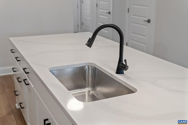 interior details with white cabinetry, sink, and hardwood / wood-style flooring