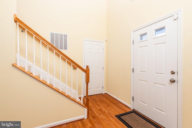 foyer entrance featuring visible vents, baseboards, stairway, light wood-type flooring, and a high ceiling