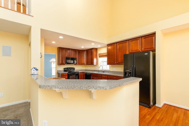 kitchen with black appliances, a breakfast bar, a high ceiling, light countertops, and baseboards