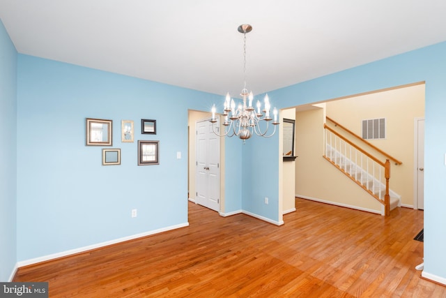 unfurnished dining area featuring visible vents, light wood-style flooring, baseboards, a chandelier, and stairs