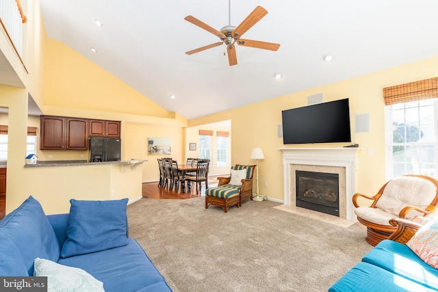 carpeted living area with a wealth of natural light, a premium fireplace, high vaulted ceiling, and a ceiling fan