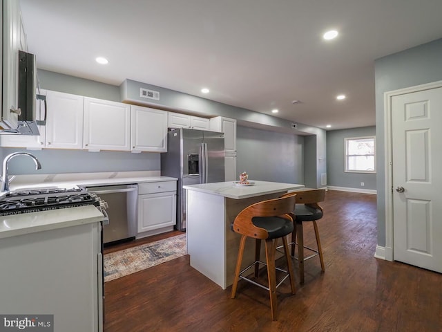 kitchen with stainless steel appliances, dark wood-type flooring, white cabinetry, a kitchen island, and a breakfast bar area