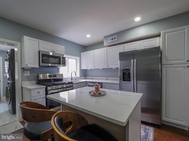 kitchen with dark hardwood / wood-style floors, appliances with stainless steel finishes, stacked washer / drying machine, a kitchen island, and white cabinetry