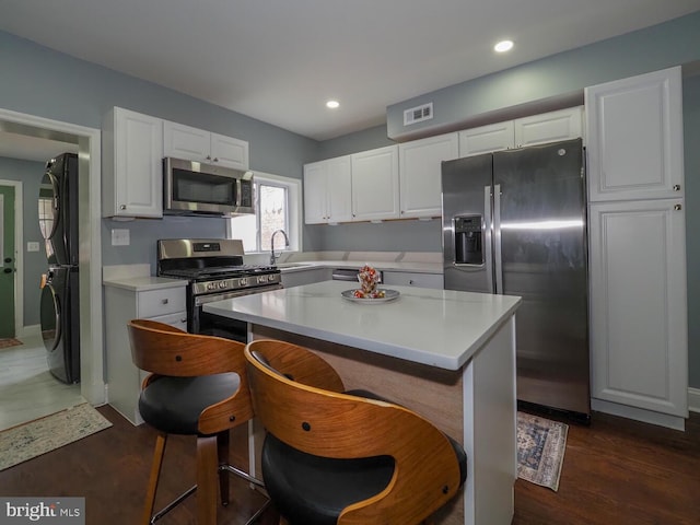 kitchen with dark wood-type flooring, white cabinets, appliances with stainless steel finishes, a kitchen island, and stacked washer / dryer