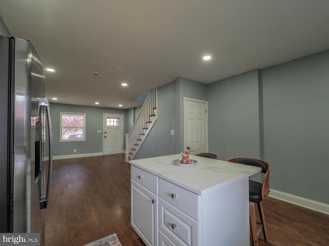 kitchen with white cabinetry, dark hardwood / wood-style flooring, stainless steel refrigerator with ice dispenser, a kitchen bar, and a kitchen island