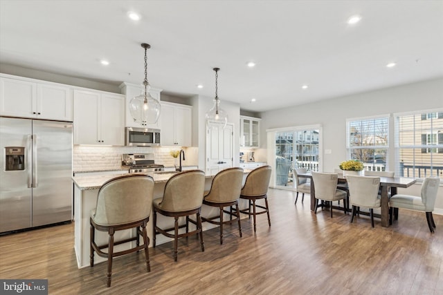 kitchen with light stone countertops, decorative light fixtures, a kitchen island with sink, white cabinets, and appliances with stainless steel finishes