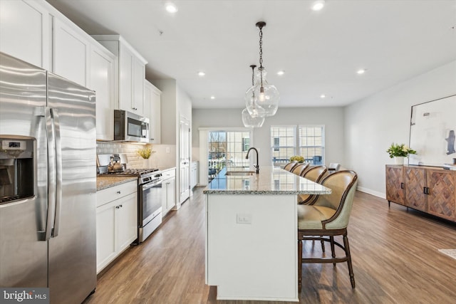 kitchen with a center island with sink, sink, light stone countertops, appliances with stainless steel finishes, and decorative light fixtures