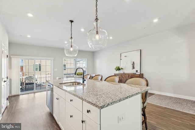 kitchen with light stone counters, sink, pendant lighting, white cabinetry, and an island with sink