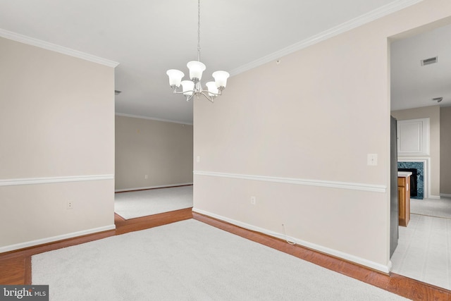 spare room featuring a chandelier, wood finished floors, visible vents, baseboards, and ornamental molding