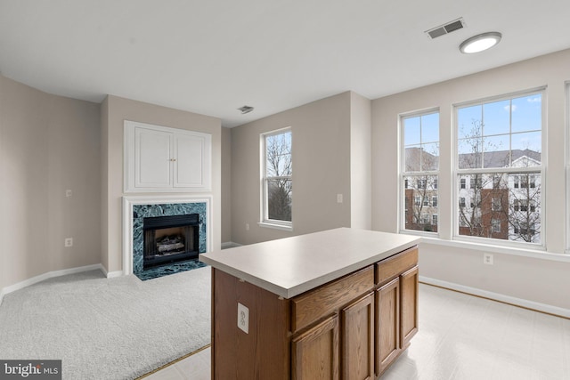 kitchen with a fireplace, a kitchen island, visible vents, baseboards, and light countertops