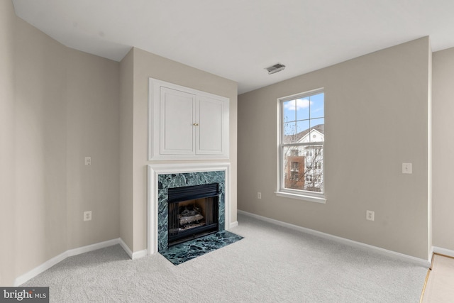 unfurnished living room with carpet floors, a premium fireplace, visible vents, and baseboards