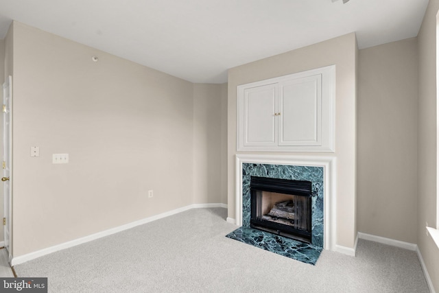 unfurnished living room with a high end fireplace, baseboards, and carpet