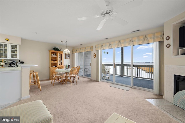 dining room with a tile fireplace, ceiling fan, and light colored carpet