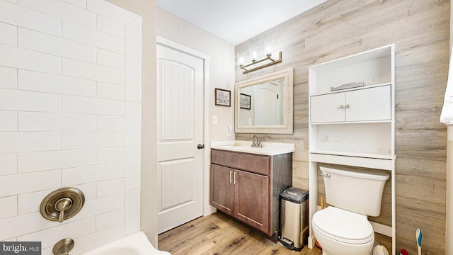 bathroom with wood-type flooring, vanity, toilet, and tile walls