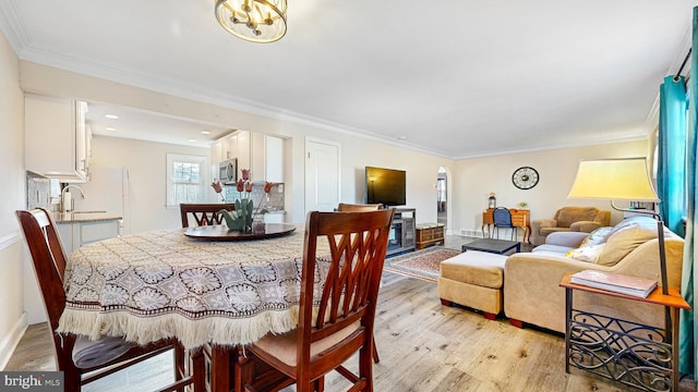 dining area featuring sink, light wood-type flooring, ornamental molding, and an inviting chandelier