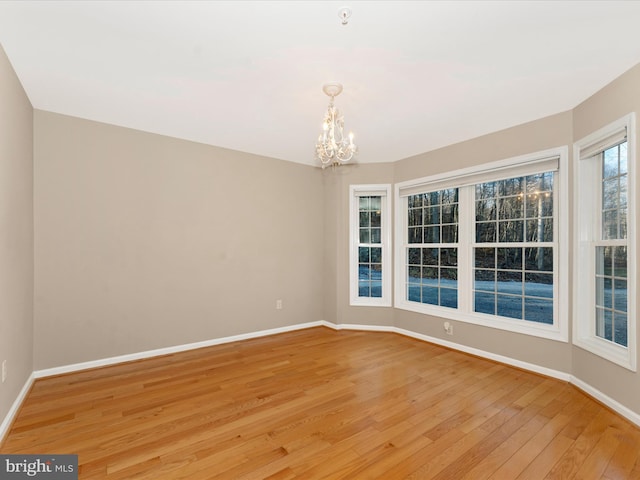 empty room with a notable chandelier and light hardwood / wood-style floors