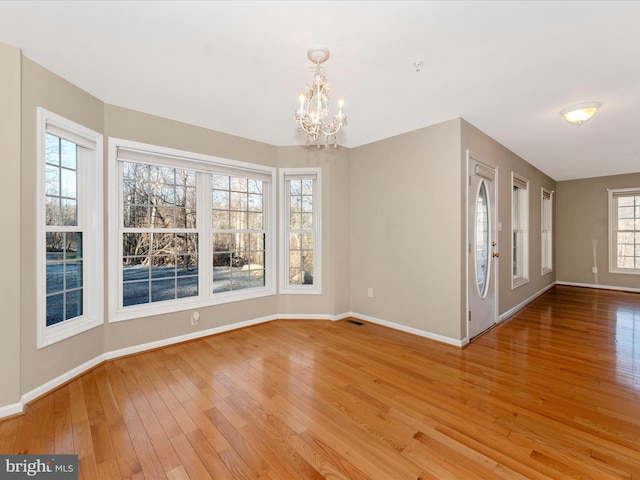 unfurnished room featuring a chandelier, light wood-type flooring, and plenty of natural light