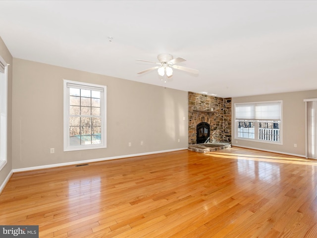 unfurnished living room with light hardwood / wood-style floors, a stone fireplace, and a healthy amount of sunlight