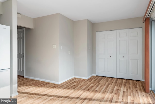 unfurnished bedroom with a closet, white refrigerator, and light hardwood / wood-style flooring