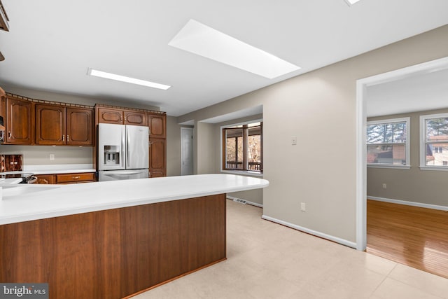 kitchen with kitchen peninsula, stainless steel fridge, light wood-type flooring, a skylight, and sink