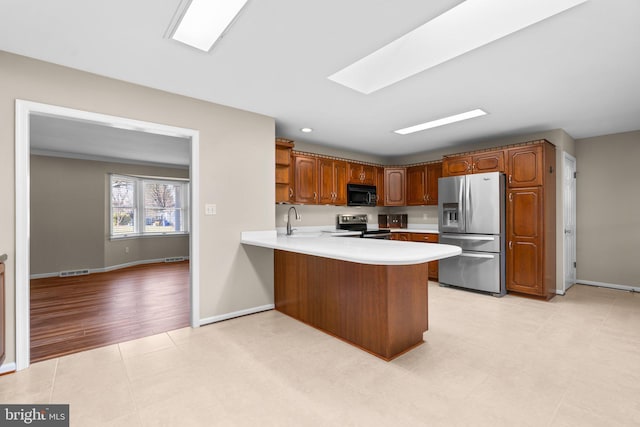 kitchen featuring sink, a skylight, appliances with stainless steel finishes, light hardwood / wood-style floors, and kitchen peninsula