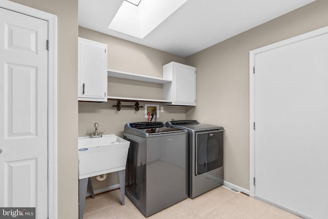 clothes washing area featuring washer and clothes dryer, cabinets, light tile patterned floors, and a skylight