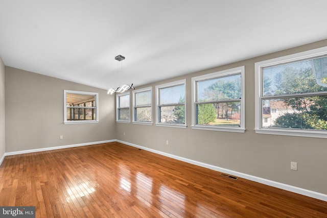 empty room featuring hardwood / wood-style floors, vaulted ceiling, and an inviting chandelier