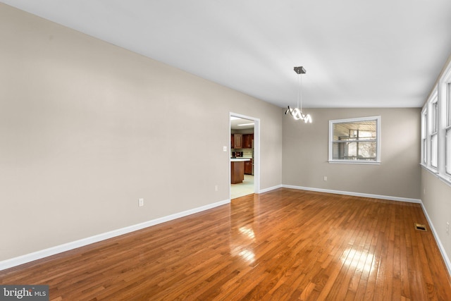 unfurnished room with hardwood / wood-style floors, vaulted ceiling, and an inviting chandelier