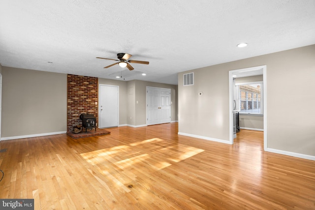 unfurnished living room with ceiling fan, light wood-type flooring, a wood stove, and a textured ceiling