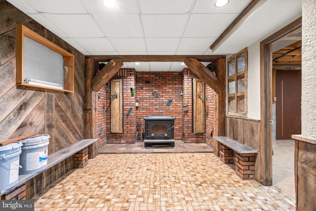 unfurnished living room with a paneled ceiling, wood walls, and a wood stove